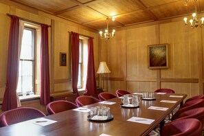 Ett konferensrum med träpanel på väggarna, röda draperier, en kristallkrona och en tavla på väggen.