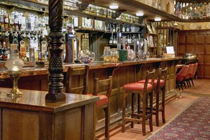 Eine Bar mit Holzhockern, einer Auswahl an Spirituosenflaschen und verschiedenen Gläsern.