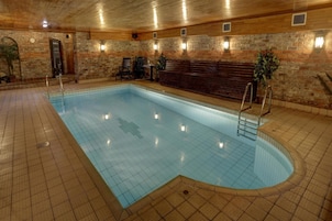 Una piscina interior con cubierta de madera, un banco y luces empotradas.