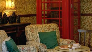 A room with a floral patterned sofa, a red telephone booth, a table with a cup and pastries, and a lamp on the wall. - The Bell In Driffield (Driffield)
