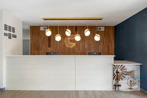 A reception desk with a wooden panel wall, a white counter, and a windmill artwork.