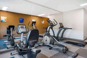 Un gimnasio con varios equipos de ejercicio, incluyendo cintas de correr, una elíptica y una bicicleta estática, todo con la marca 'TRUE'.