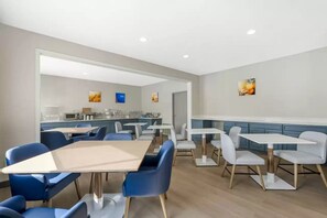 A modern dining area with blue and white chairs, a central table, and a kitchen in the background.