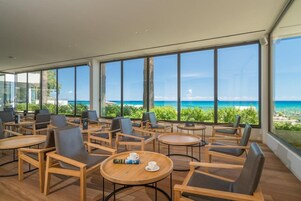 Un área de estar moderna en el interior con amplios ventanales con vista a una playa.