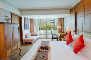 A hotel room with a bed, a sofa, a desk, and a view of a balcony with flowers. - Royal President Bangkok (Bangkok)