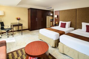 Quarto de hotel com duas camas, uma escrivaninha, uma cadeira, uma mesinha e um guarda-roupa.