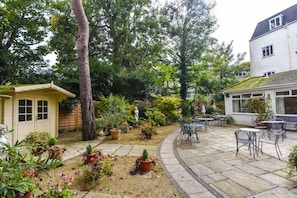 A patio area with outdoor seating, a small garden, and a white building with a sloped roof. - Mayfair Hotel - Oceana Collection (Bournemouth)