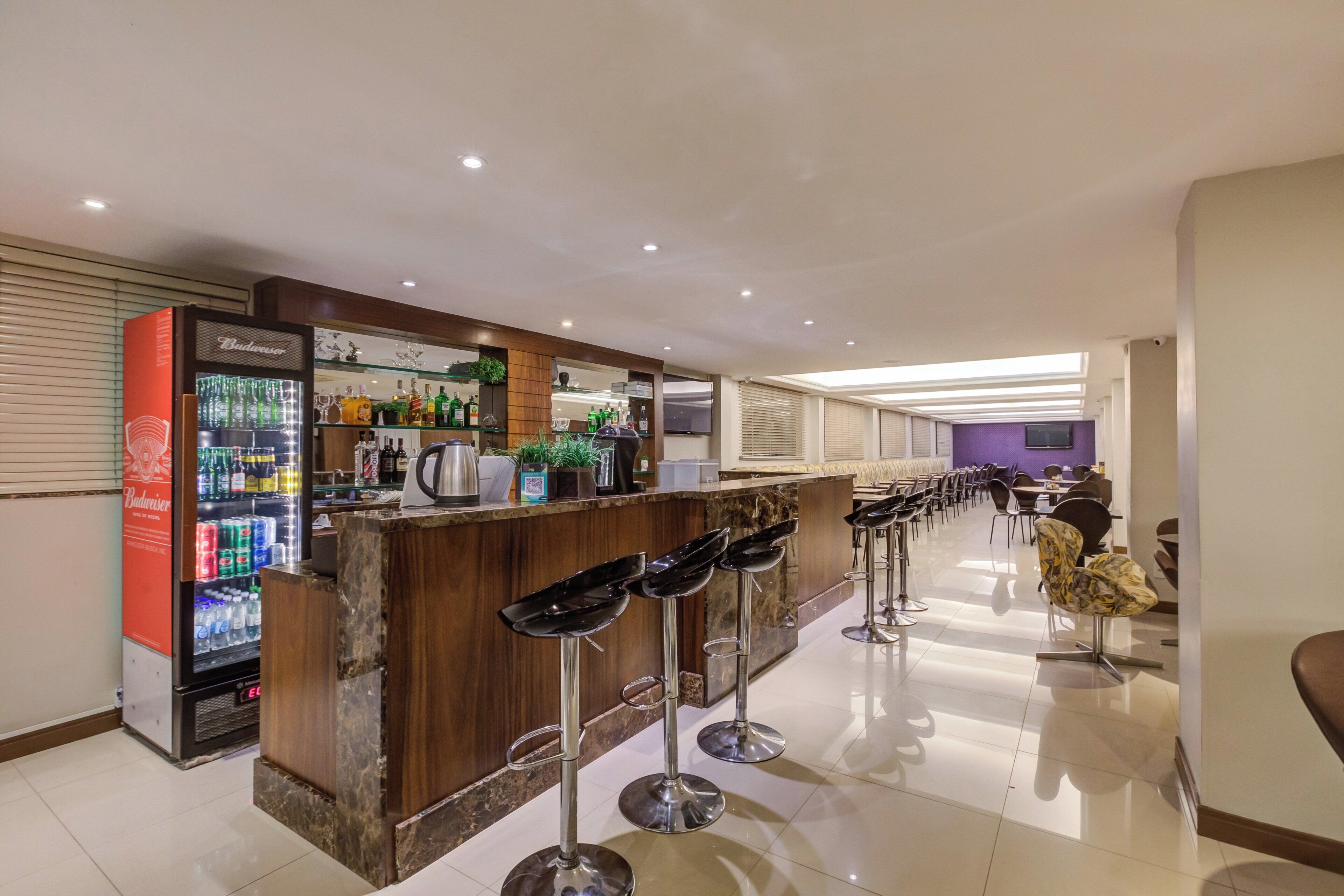 A bar area with stools, a refrigerator stocked with beverages, and a counter with various items.