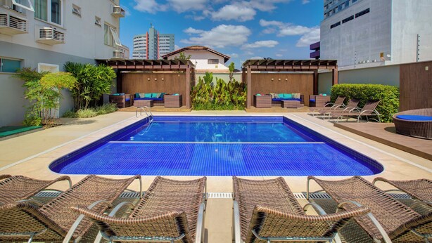 A swimming pool with lounge chairs, a small garden area, and a view of surrounding buildings. - Slim Joinville By Slaviero Hoteis (Joinville)