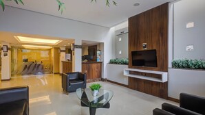 A modern hotel lobby with a reception desk, seating area, and a television mounted on a wooden wall. - Slim Joinville By Slaviero Hoteis (Joinville)