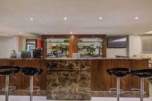 Eine Bar mit Marmorarbeitsplatte, Barhocker und einer Auswahl an Flaschen und Gläsern.