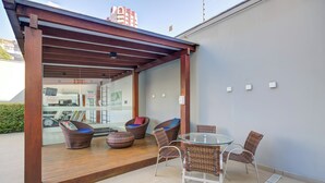 A covered outdoor seating area with wicker furniture, a glass table, and a view into the building. - Slim Joinville By Slaviero Hoteis (Joinville)