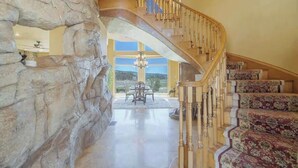A grand staircase with a wooden handrail, leading to a dining area with a chandelier. - Big Bear Lakefront Luxury Home w/ Spa & Views (Big Bear Lake)