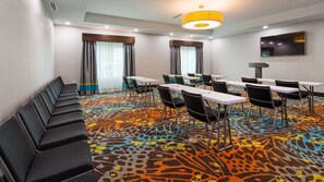A conference room with a patterned carpet, long tables, chairs, a sofa, and a TV on the wall.