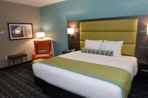 A hotel room with a large bed, a chair, a nightstand, a lamp, and a framed picture on the wall.