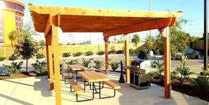 A wooden pergola with picnic tables and a barbecue grill.
