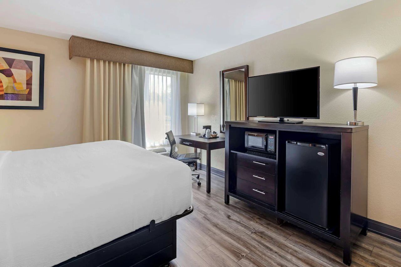 Una habitación de hotel con cama, escritorio con computadora, televisor y refrigerador.