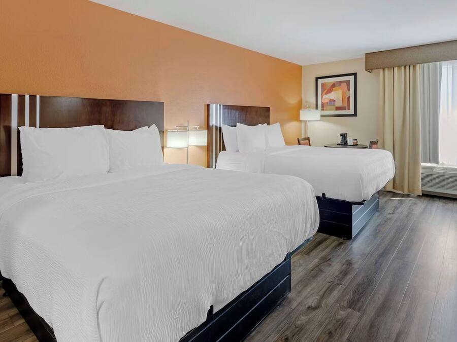 Een hotelkamer met twee bedden, een nachtkastje, een lamp en een raam met gordijnen.