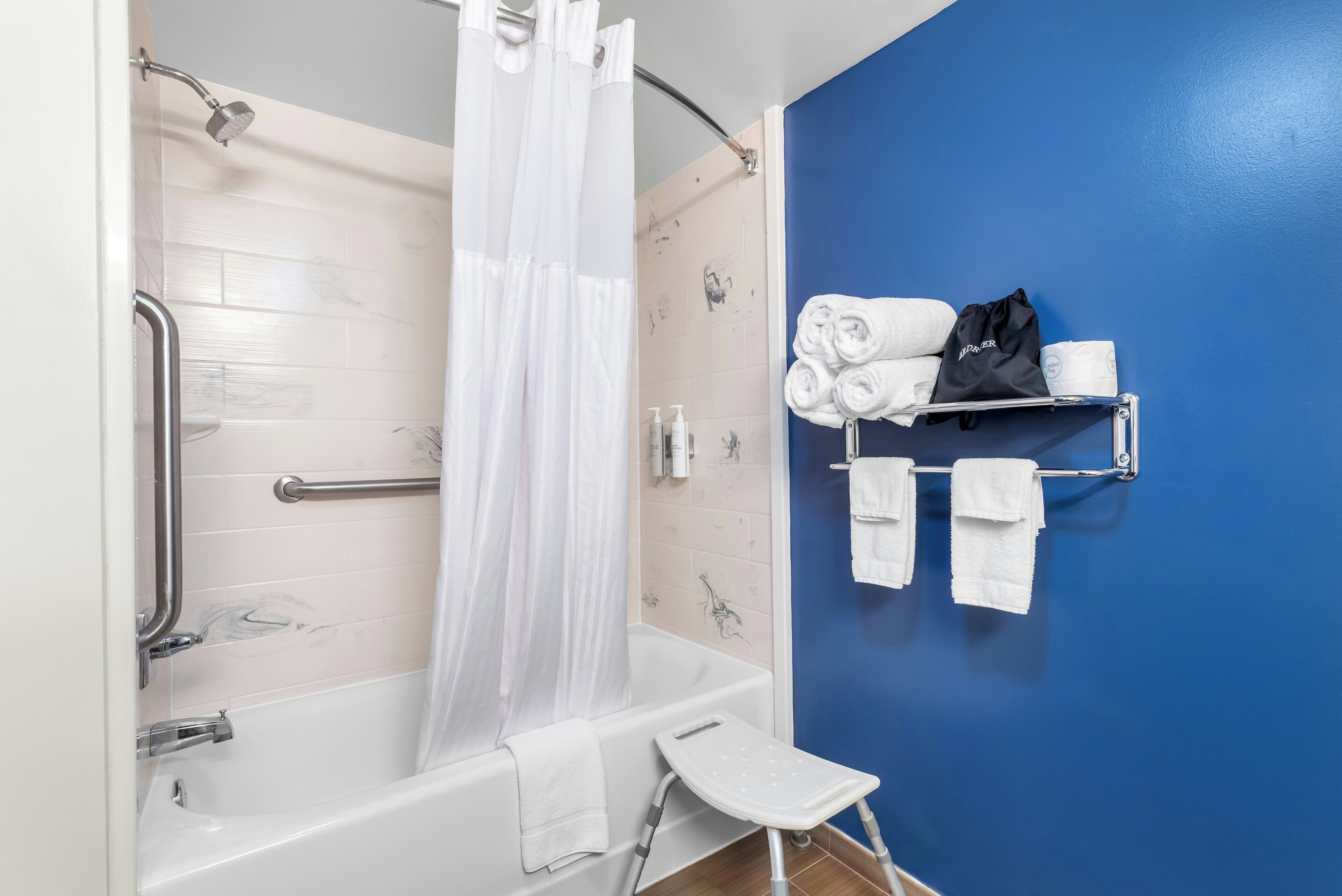 A bathroom with a bathtub, a shower curtain, a grab bar, a towel rack with towels, and a small step stool.