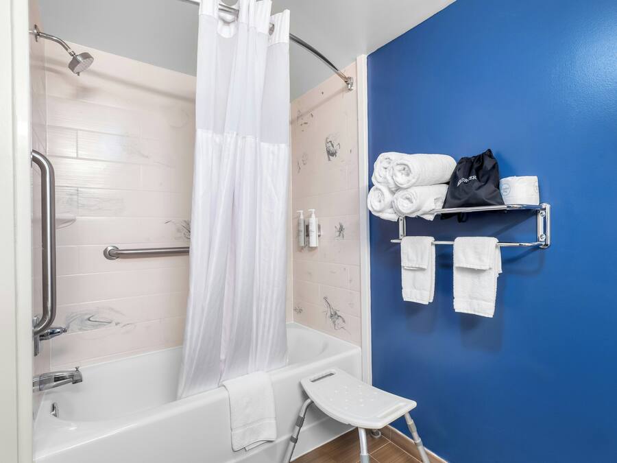 A bathroom with a bathtub, a shower curtain, a grab bar, a towel rack with towels, and a small step stool.