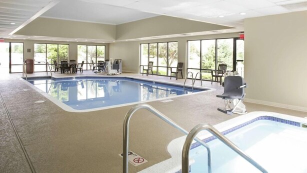 An indoor swimming pool with clear glass walls, a lounge area with chairs, and a view of the outdoors. - Chicago Elgin / I-90, IL (Elgin)