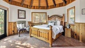Une chambre avec un plafond en bois, un grand lit, un banc et une fenêtre.