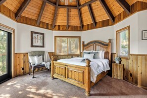 Een slaapkamer met een houten plafond, een groot bed, een bankje en een raam.