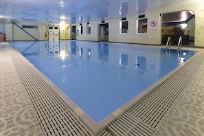 En indendørs swimmingpool med krystalklart vand og fliserede vægge, samt et skilt med forbud mod løb.