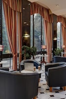 A modern lounge area with leather sofas, a laptop, and two drinks on a table. Large windows with curtains are visible.