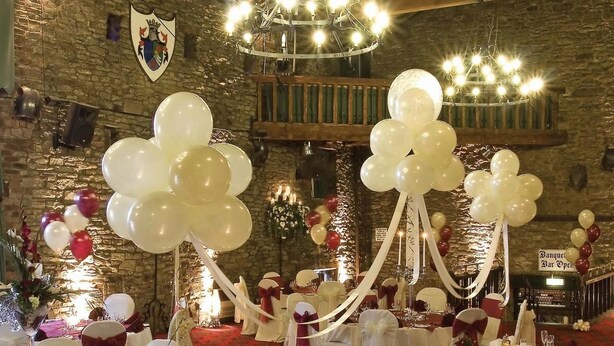 A banquet hall with long tables, white and red decorations, chandeliers, and stone walls.