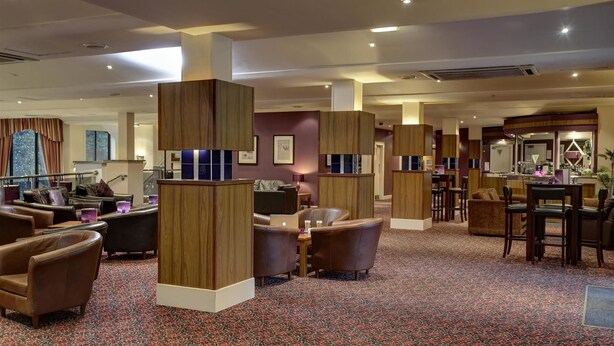 A hotel lobby with leather seating, wooden pillars, and a patterned carpet. - Park Hall Hotel (Chorley)