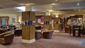 A hotel lobby with leather seating, wooden pillars, and a patterned carpet.
