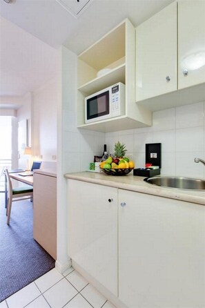 A compact kitchen with a microwave, a fruit bowl, and a sink. - Oakwood Hotel and Apartments Brisbane (Brisbane)