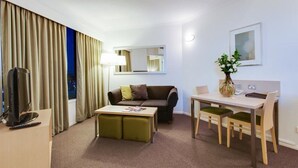 A hotel room with a sofa, a coffee table, a desk with chairs, a TV, a lamp, a mirror, and a framed picture on the wall. - Oakwood Hotel and Apartments Brisbane (Brisbane)