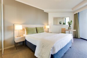 A hotel room with a large bed, two bedside lamps, a round table with a vase of flowers, and a mirror on the wall. - Oakwood Hotel and Apartments Brisbane (Brisbane)