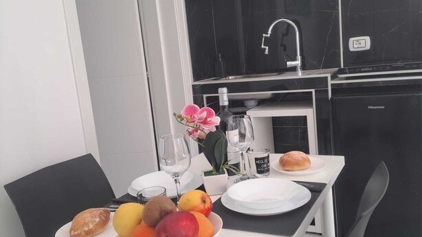 Taula de dinar amb plats, un bol de fruita i una ampolla. Hi ha un armari blanc i negre amb un rentapousa i un refrigerador Hisense.