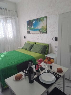 Ein Hotelzimmer mit Bett, einem Esstisch mit Frühstücksangeboten, einem Bild an der Wand und einem Fenster mit Vorhängen.