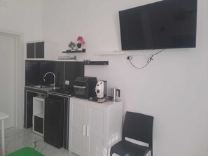 Eine kompakte Küchenzeile mit Herd, Spüle und Kaffeemaschine, ein Flachbildfernseher an der Wand und ein Stuhl.