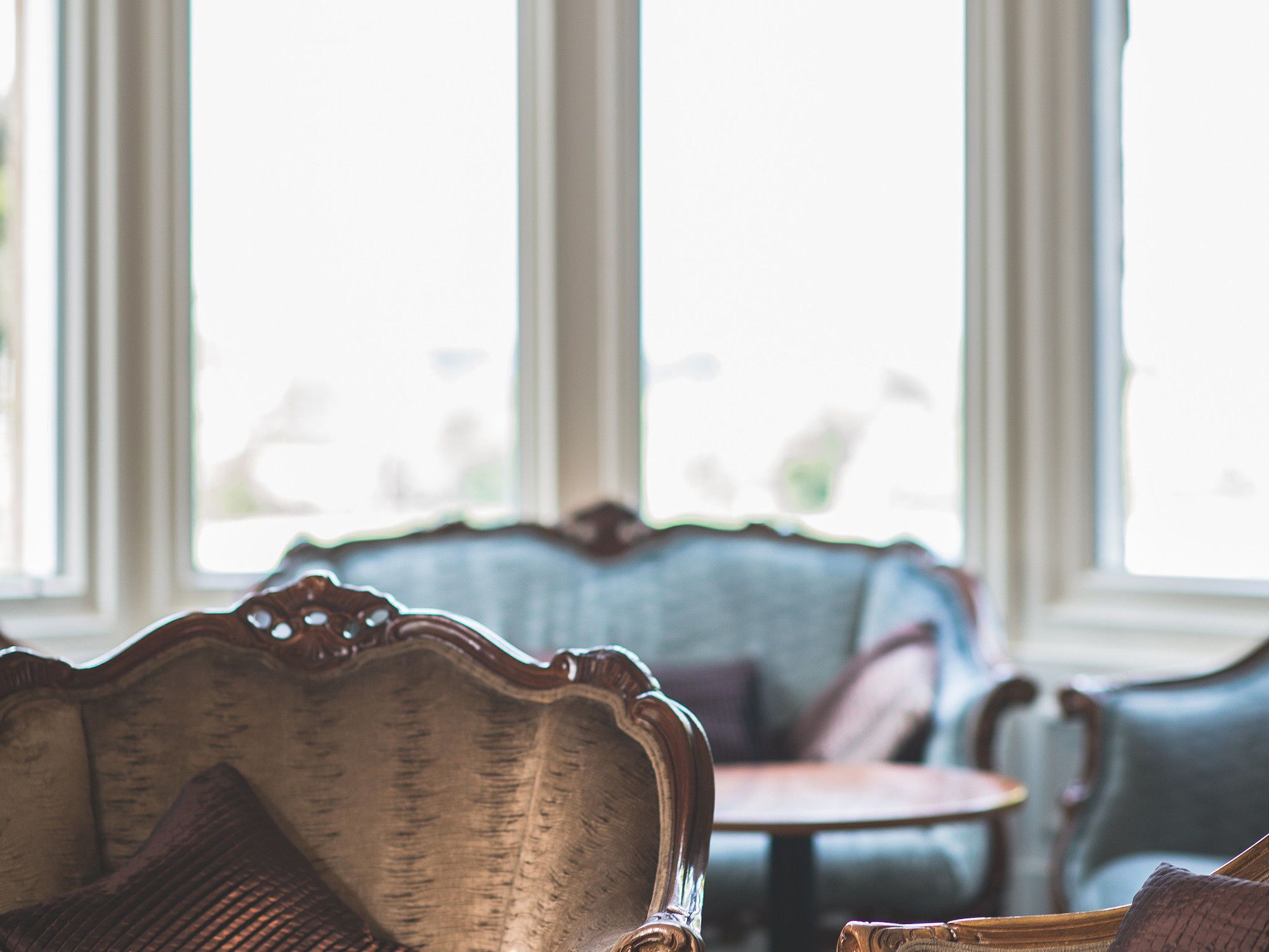 A room with a vintage sofa, a small round table, and large windows.