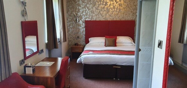 Habitación de hotel con cama, escritorio, silla, espejo y ventana.