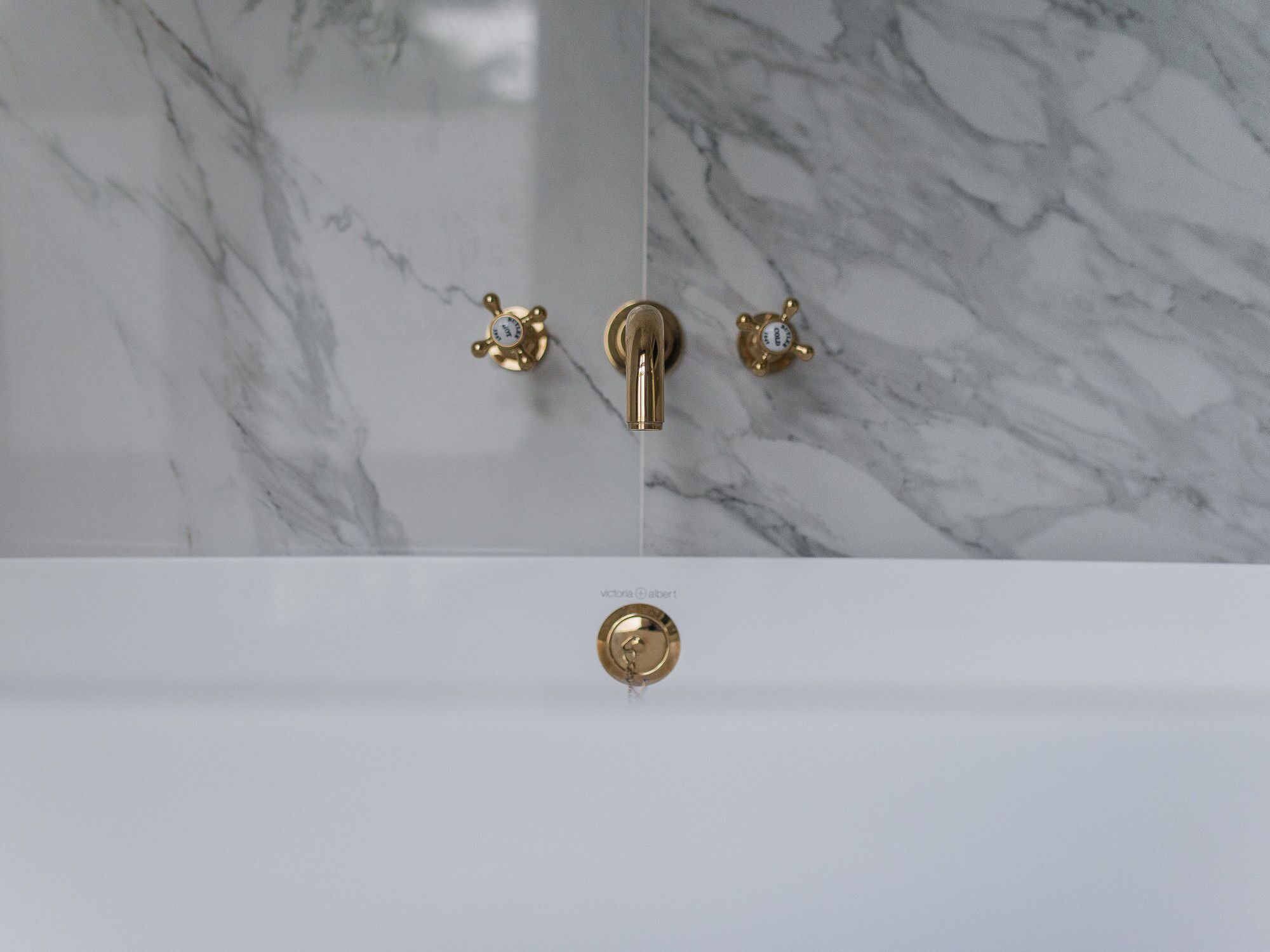 Une salle de bain avec un mur en marbre, un robinet doré et une poignée dorée.