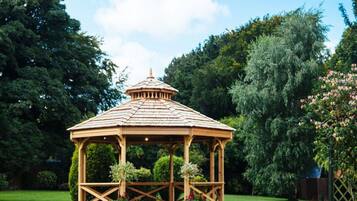 A wooden gazebo with a tiled roof, surrounded by a well-maintained lawn and dense trees.