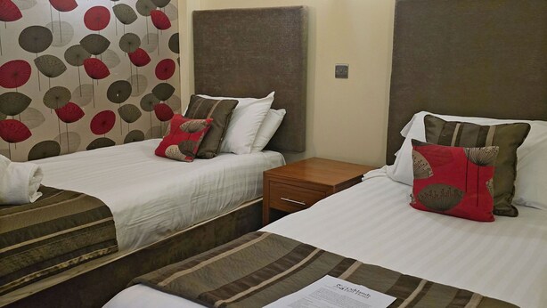 Habitación de hotel con dos camas, cada una con una almohada y una mesita de noche de madera.