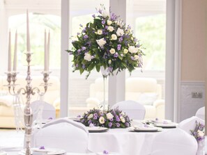Una mesa dispuesta para un evento formal, con un centro de mesa floral, manteles blancos y candelabros.