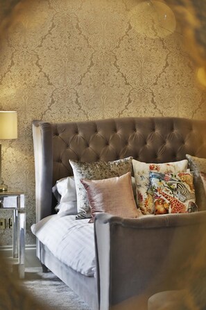 Cama con cabecera capitonada, almohadas decorativas y pared con estampado.