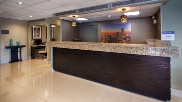 Un mostrador de recepción de hotel con un mural de la ciudad, una zona de recepción y un cartel que indica 'Best Western' y 'SNO Hospitality'.