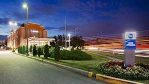 Et Best Western hotel med moderne design, en parkeringsplads og en vej med lyseffekter, der viser trafik.
