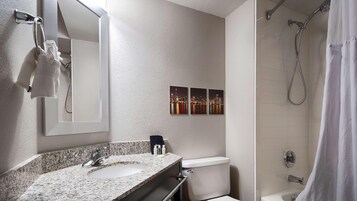 Un baño con encimera de granito, lavamanos, inodoro, ducha con cortina y espejo.