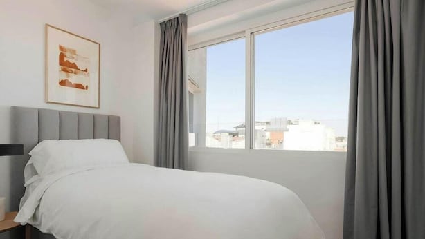 A hotel room with a bed, a bedside table, a window with curtains, and a framed picture on the wall. - Sonder Santa Ana (Madrid)