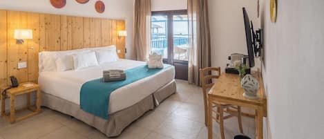 A hotel room with a large bed, a wooden headboard, a desk with a chair, and a balcony with a view.